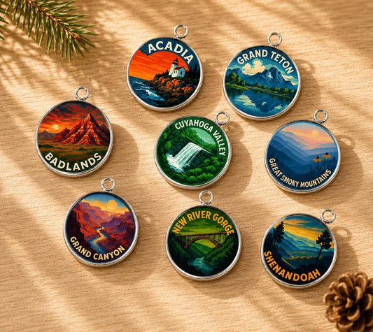 May include: Eight circular silver-toned metal charms featuring colorful landscape illustrations of U.S. National Parks. Each charm displays a specific park name including Acadia, Grand Teton, Badlands, Cuyahoga Valley, Great Smoky Mountains, Grand Canyon, New River Gorge, and Shenandoah.